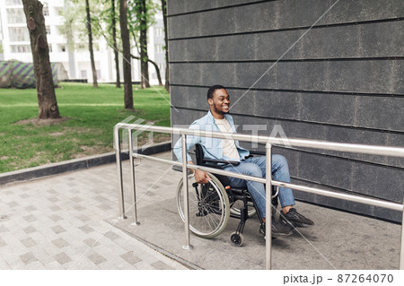 Accessible environment for people with special needs concept. Positive young black man in wheelchair using ramp outdoors